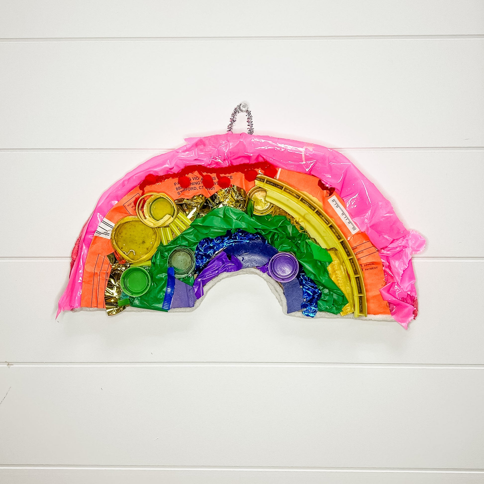 Rainbow-shaped craft made from recycled plastic bottles on a white wooden background